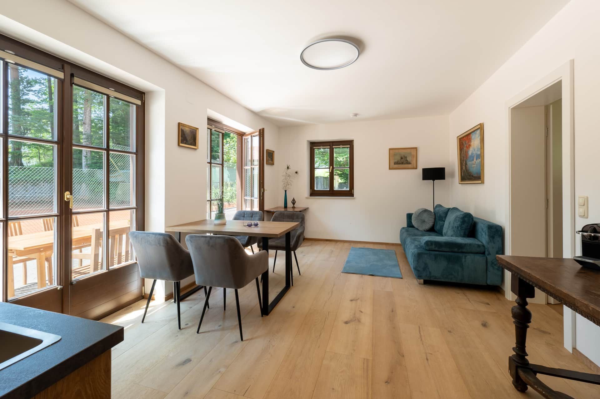 Moderne Wohnatmosphäre erleben: Ankommen und Wohlfühlen am Wolfgangsee Ferienwohnung St. Wolfgang am Wolfgangsee: Heller Wohn-Essbereich mit Samtsofa, Holztisch, Parkett & Terrassenzugang.